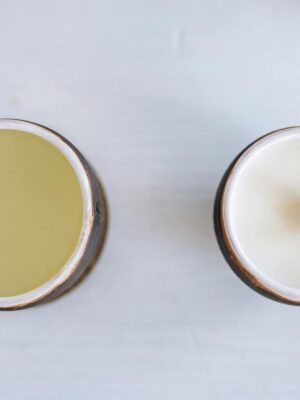 A close-up of two handmade candles in ceramic cups on a white background, showcasing different wicks.