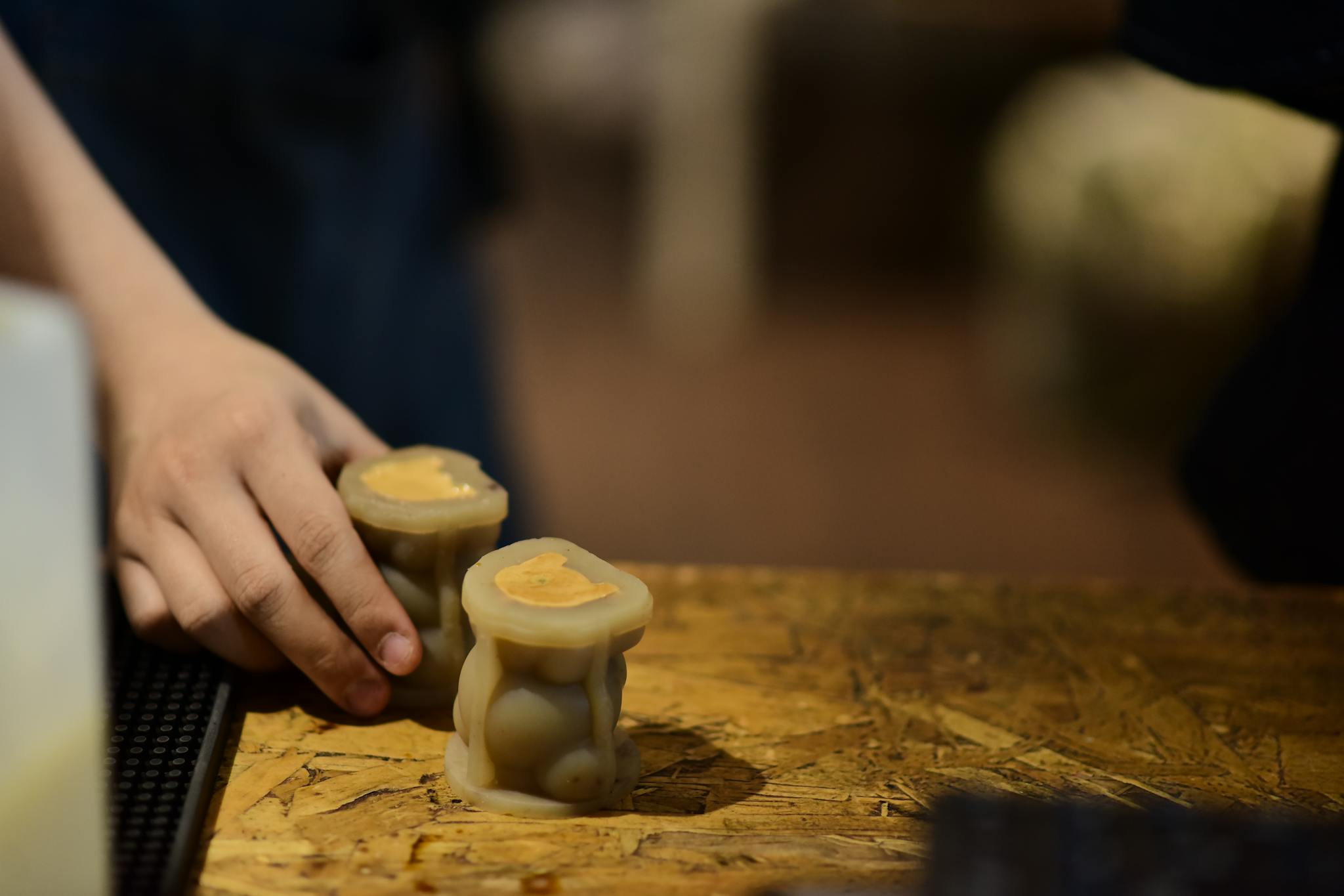 Close-up of a hand holding two homemade scented candles on a wooden surface.
